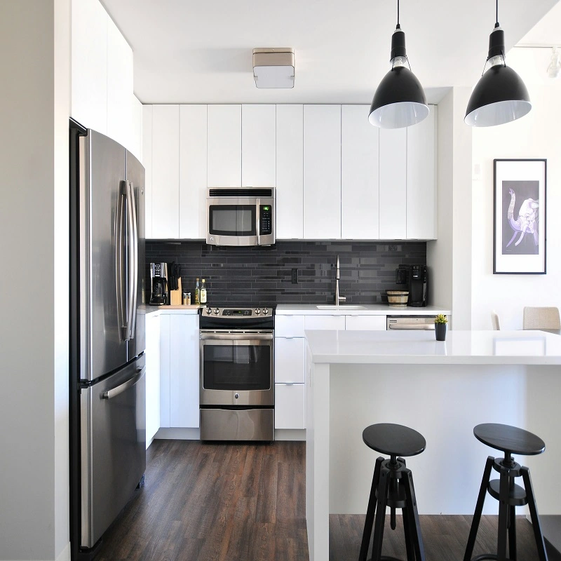 Cocina moderna con muebles blancos en acabado brillante, isla central con encimera blanca, electrodomésticos empotrados en acero inoxidable, salpicadero gris oscuro y diseño minimalista con iluminación colgante